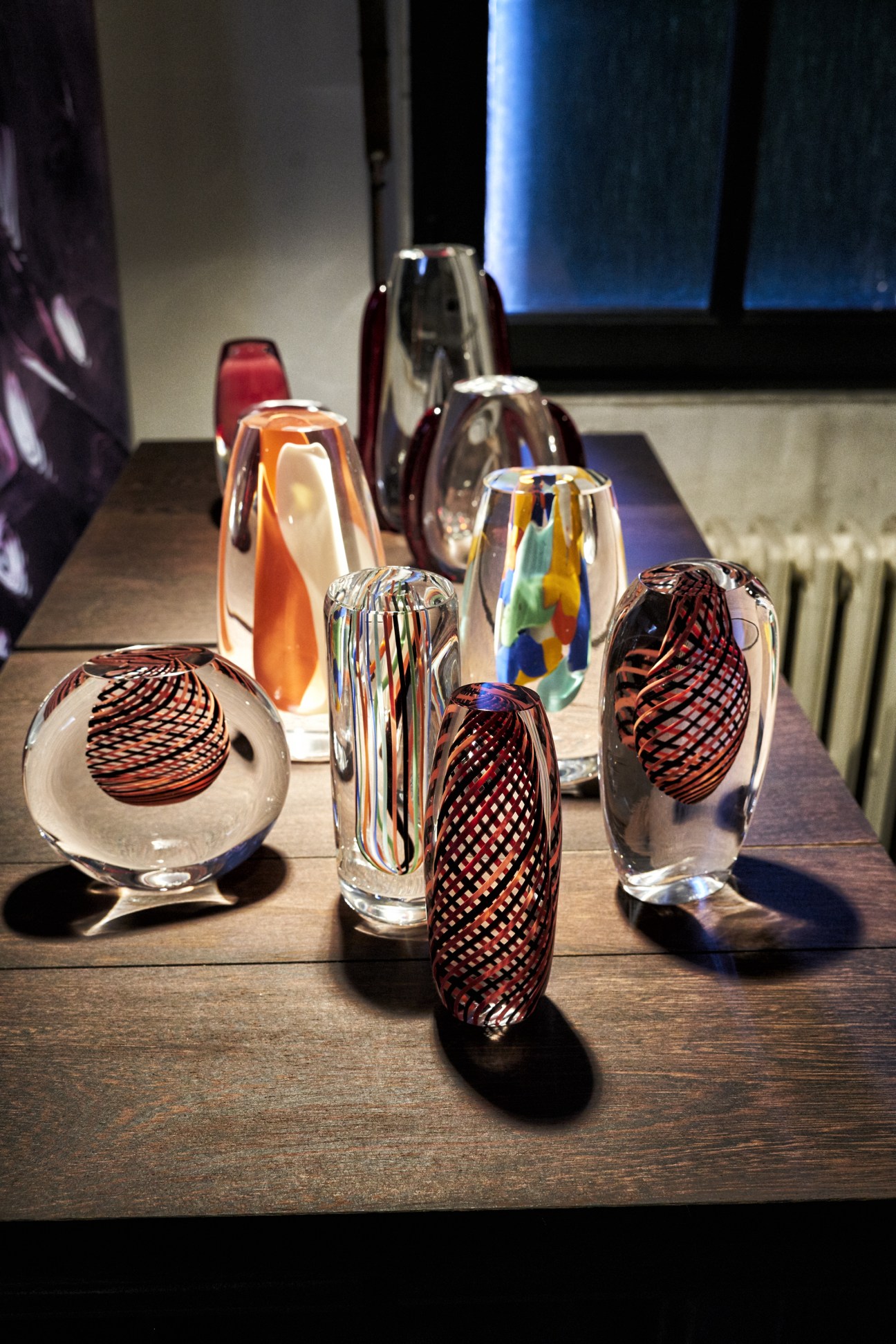 Display of Carlo Moretti glass vases in various colors and geometric patterns on a dark surface.
