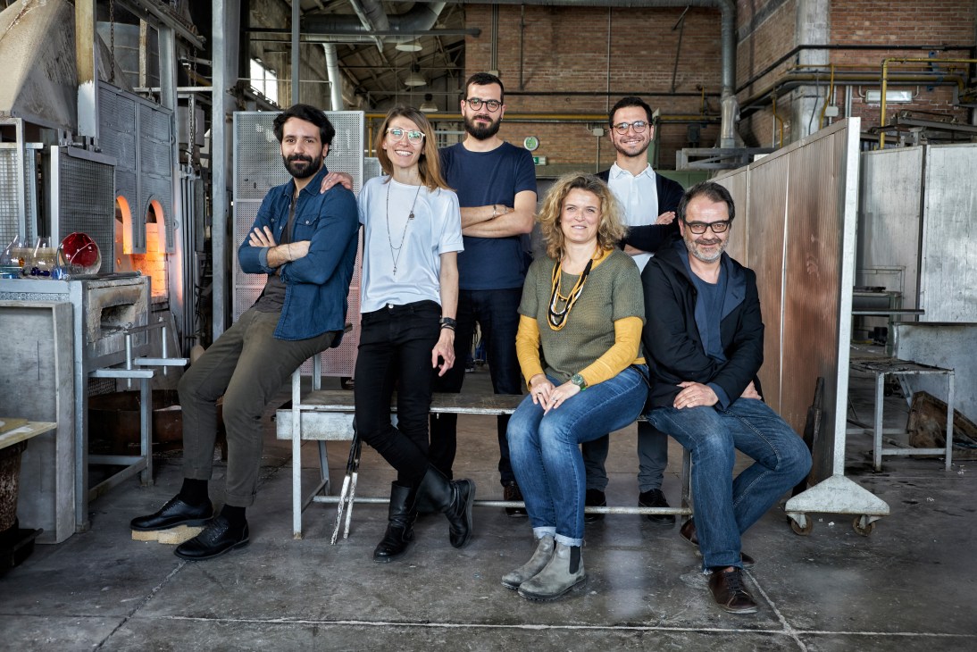 Breaking the Mould collective and Salviati's Monica Crescente pose in a glass-blowing workshop with furnaces visible in background.