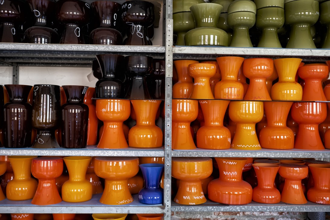 Metal shelving displaying colorful Murano glass vases in orange, yellow, brown and olive green.