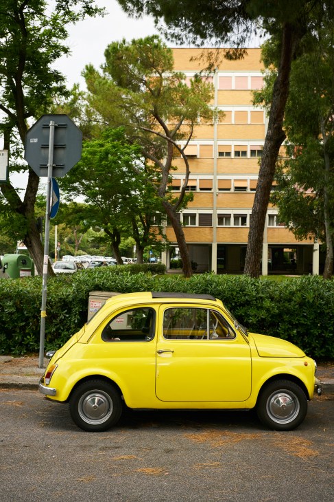 A yellow Fiat 600 D parked in front of modernist apartment building with piloti columns in Rome's Villaggio Olimpico.