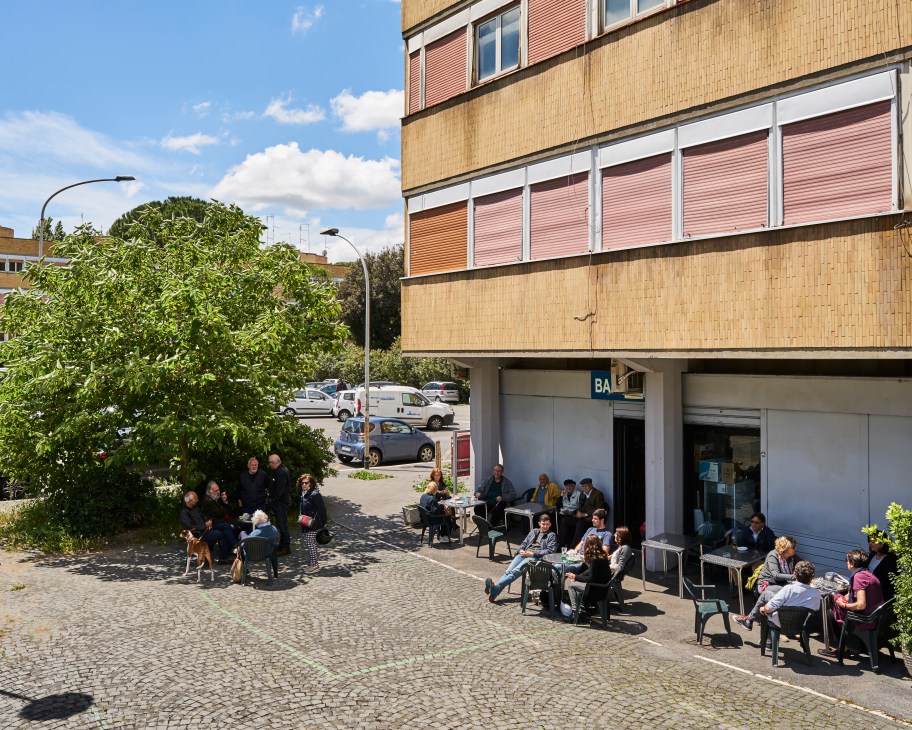Residents gather at an outdoor bar beneath a modernist apartment building on Piazza Grecia in Rome's Olympic Village.