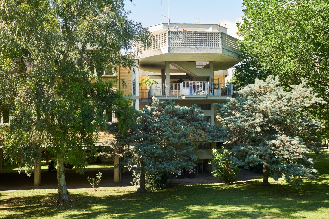 Modernist apartment building with piloti supports surrounded by lush green trees and landscaping at Rome's Villaggio Olimpico.
