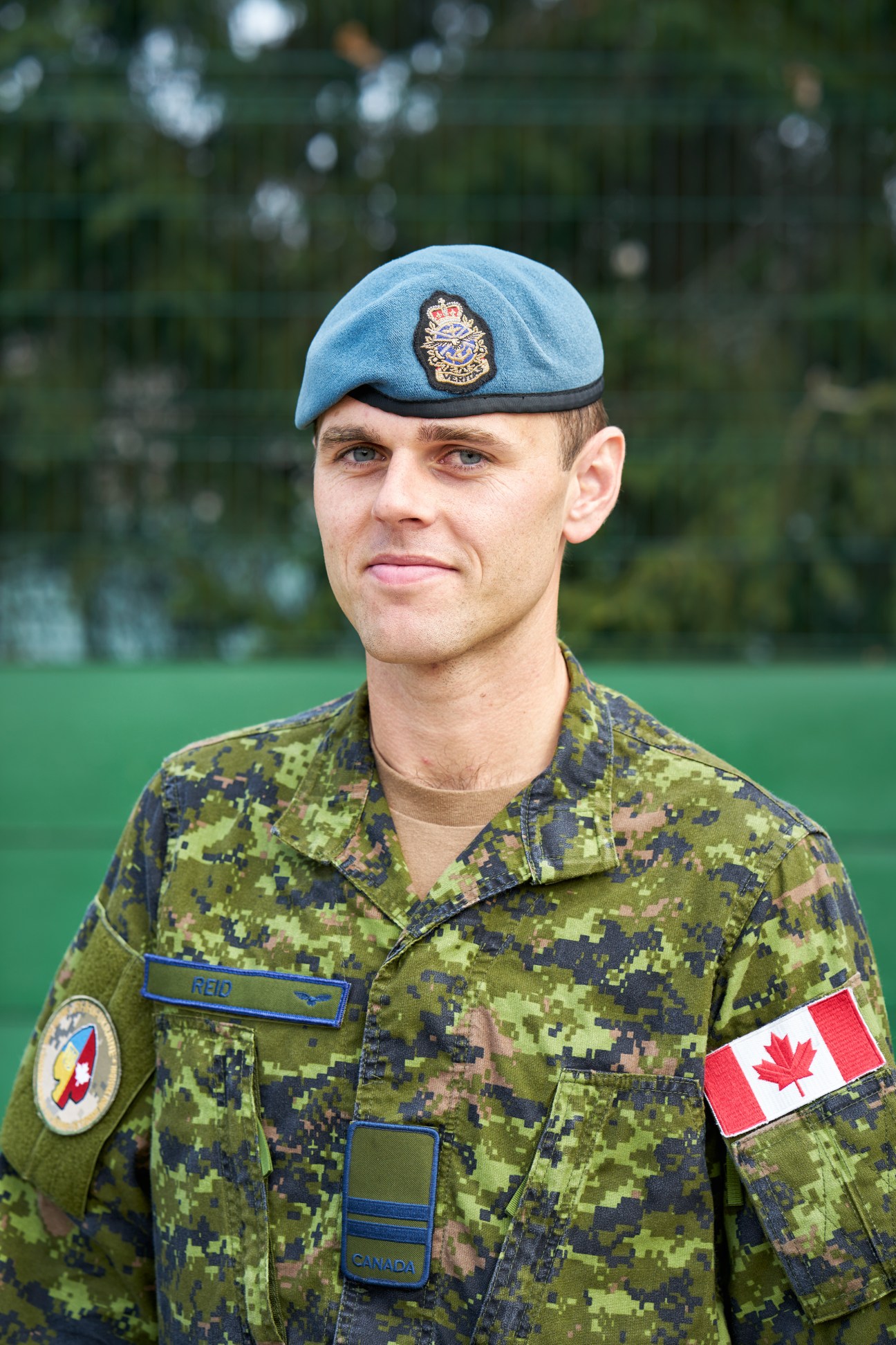 Canadian soldier in blue beret and camouflage uniform with name tag 'REID' and Canadian flag patch
