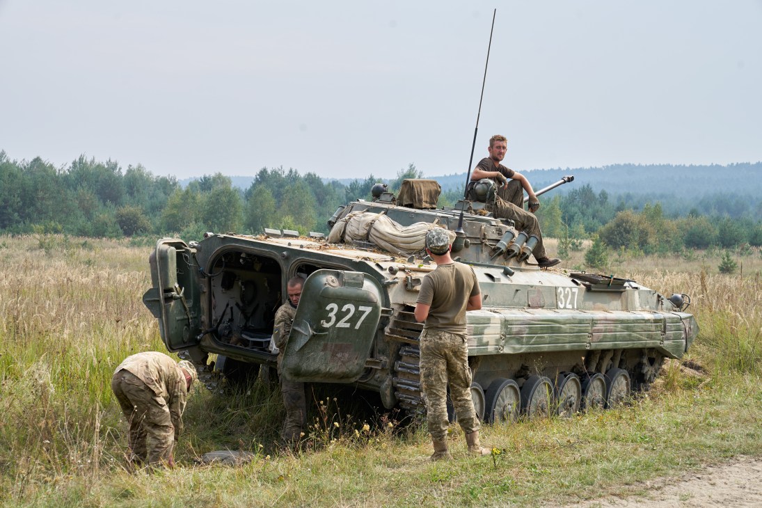 Ukrainian soldiers refuel a green military armored vehicle numbered 327 in a grassy field