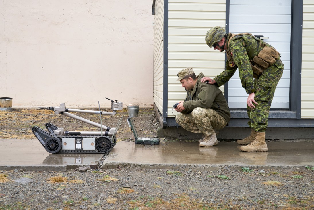 Two soldiers operating an iRobot 510 PackBot tracked robot at a military demining training facility
