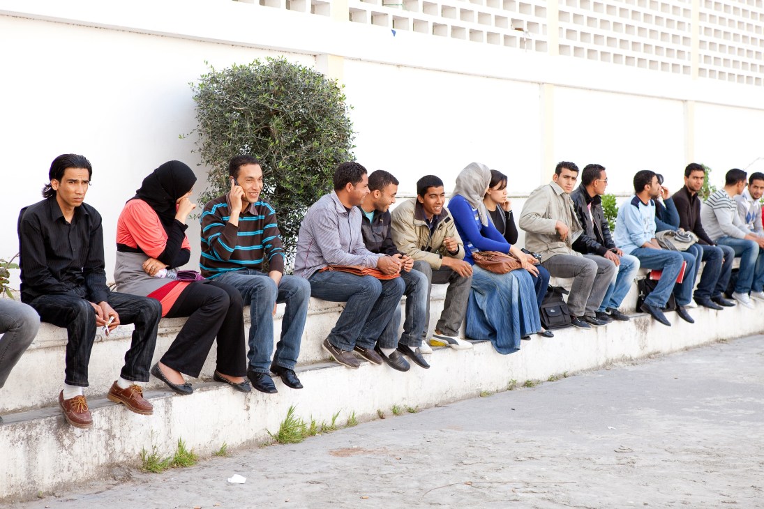 University of Tunis students sitting on a concrete ledge against a white building wall.