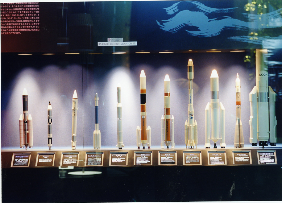 Display of rocket models from various space programs arranged on a lit museum shelf.