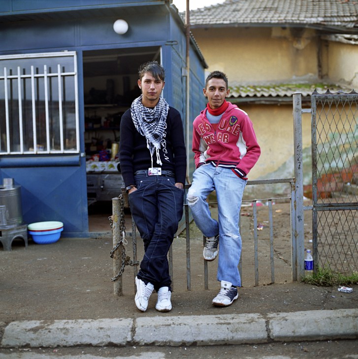 Two young men pose outside a blue structure in a Roma district near Pristina, Kosovo.