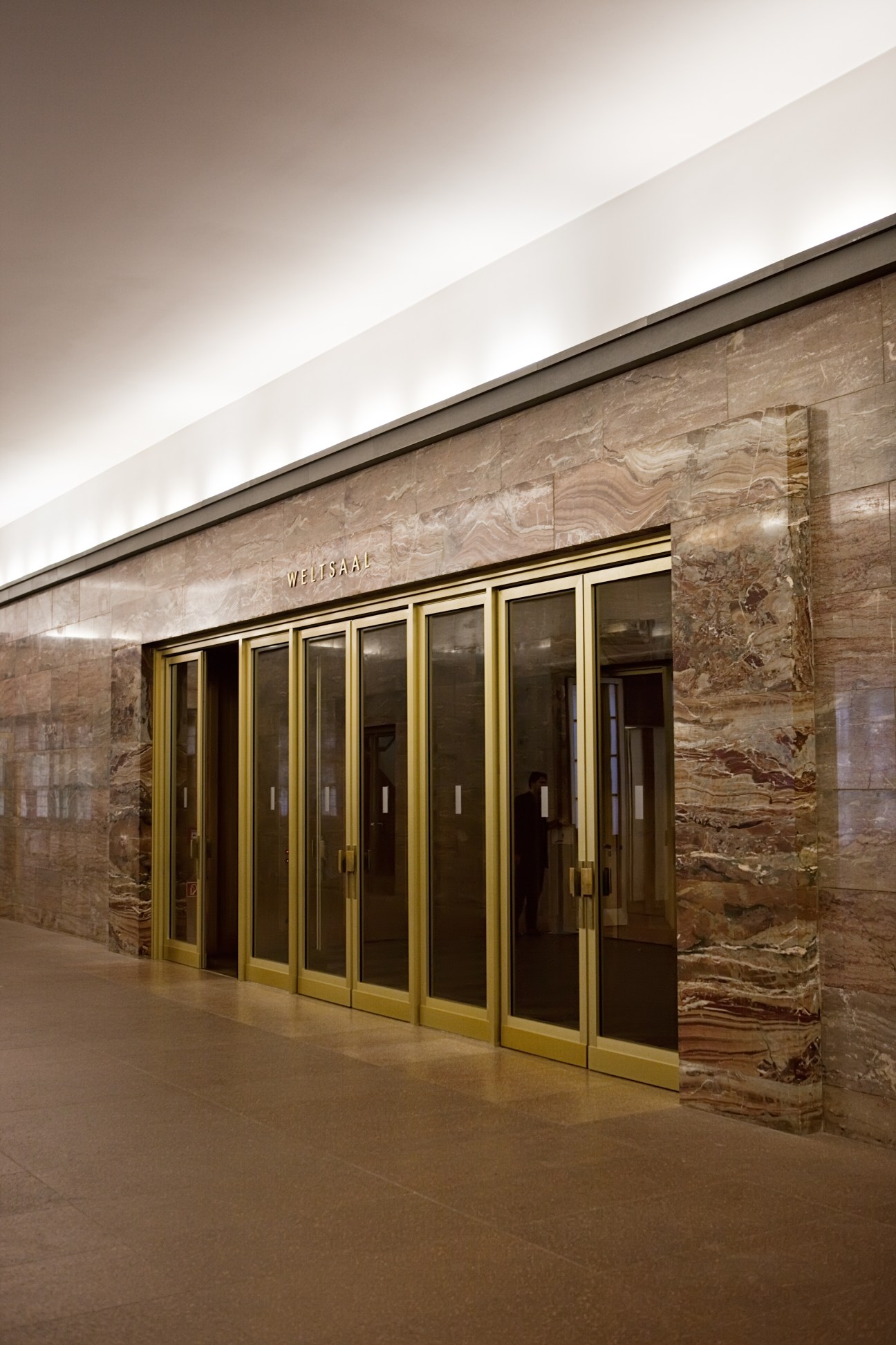 Entrance to the Weltsaal with brass-framed glass doors and textured stone walls.
