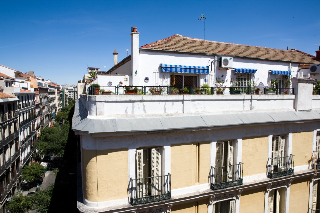 Madrid rooftop with white building featuring blue-striped awnings and terrace overlooking historic neighborhood streets.