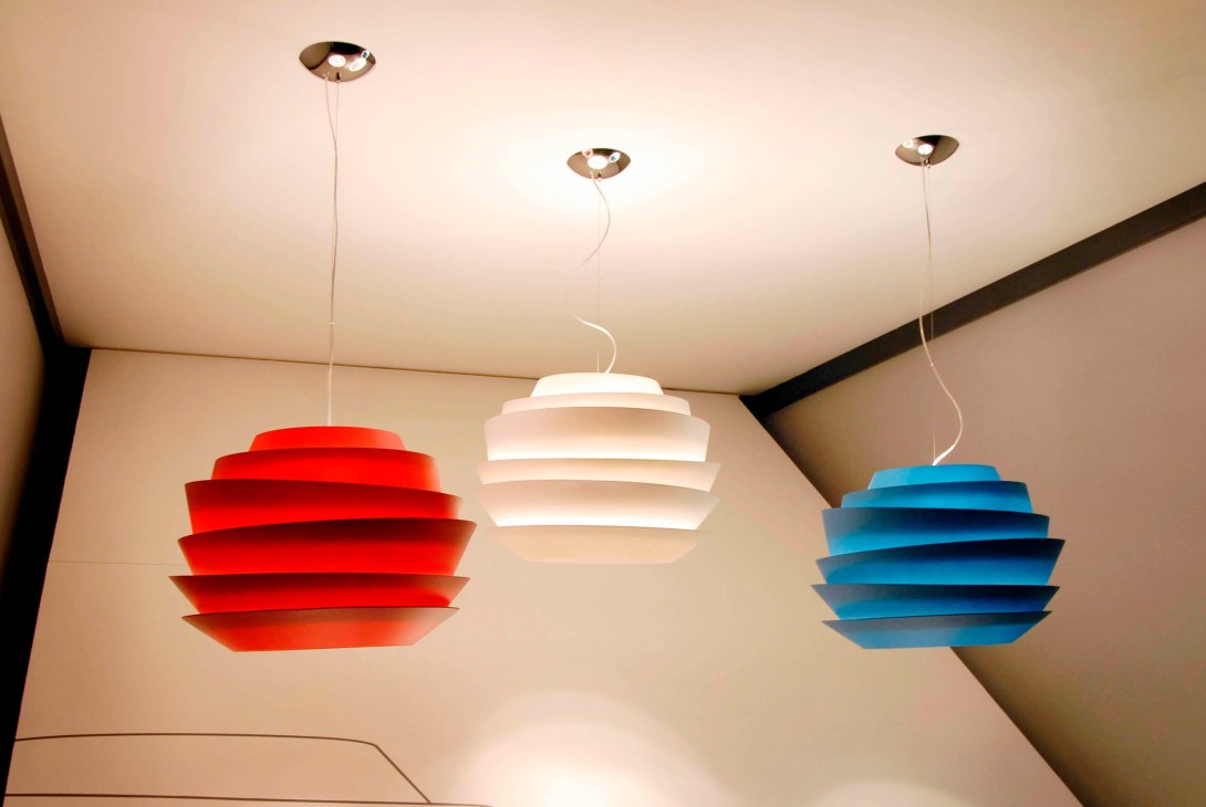 Three pendant lights with stacked disc shades in red, white, and blue hanging from a ceiling.