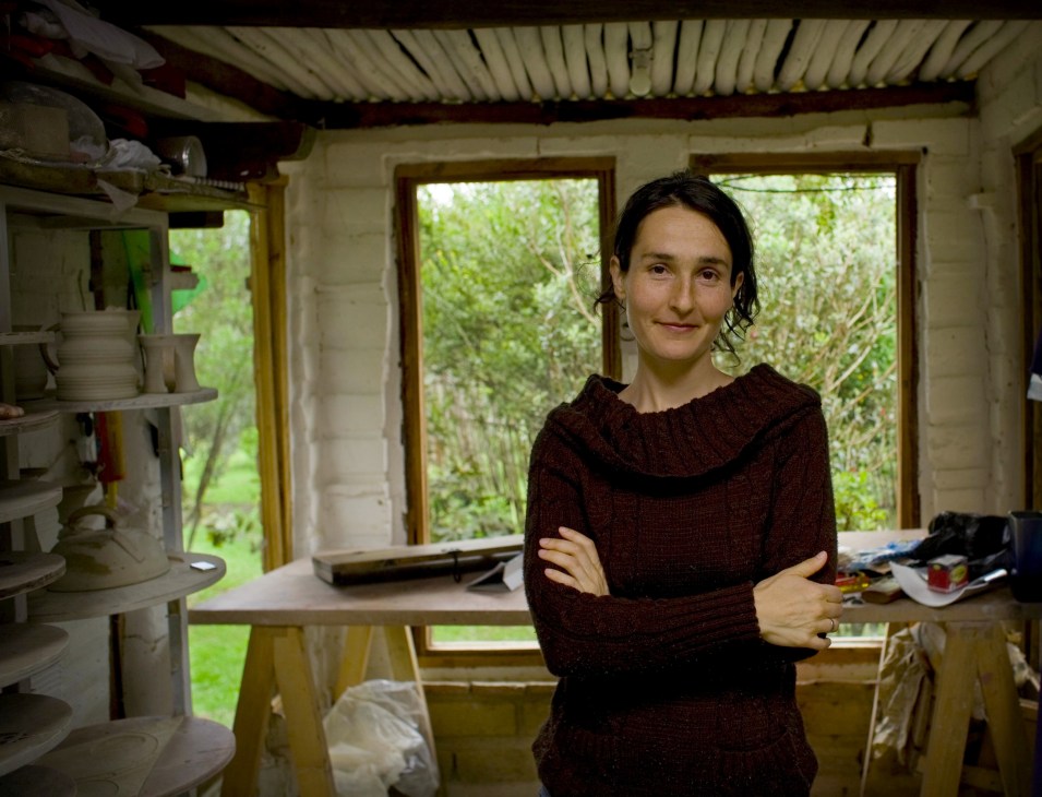 Artist Margarita Casas stands in her studio with large windows overlooking green countryside.
