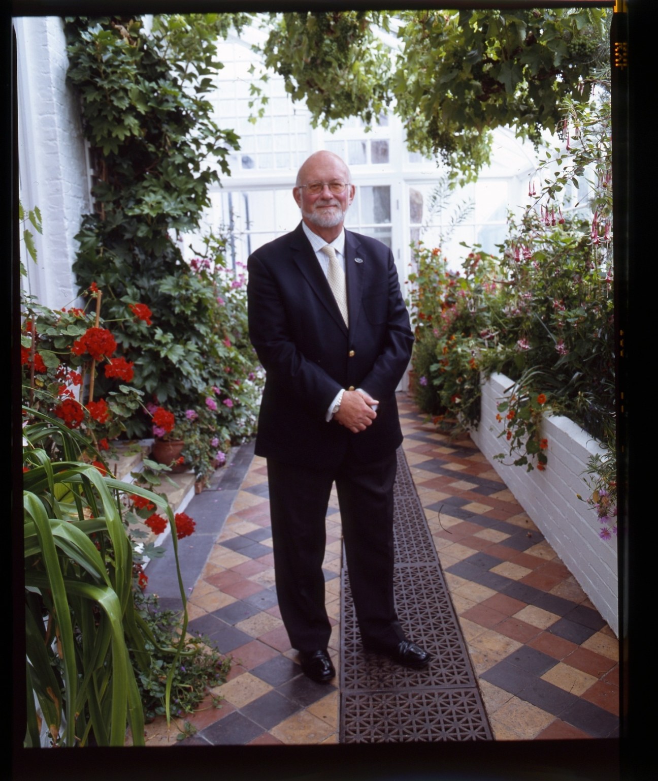 Falkland Islands governor Alan Huckle stands in a greenhouse corridor surrounded by flowering plants.