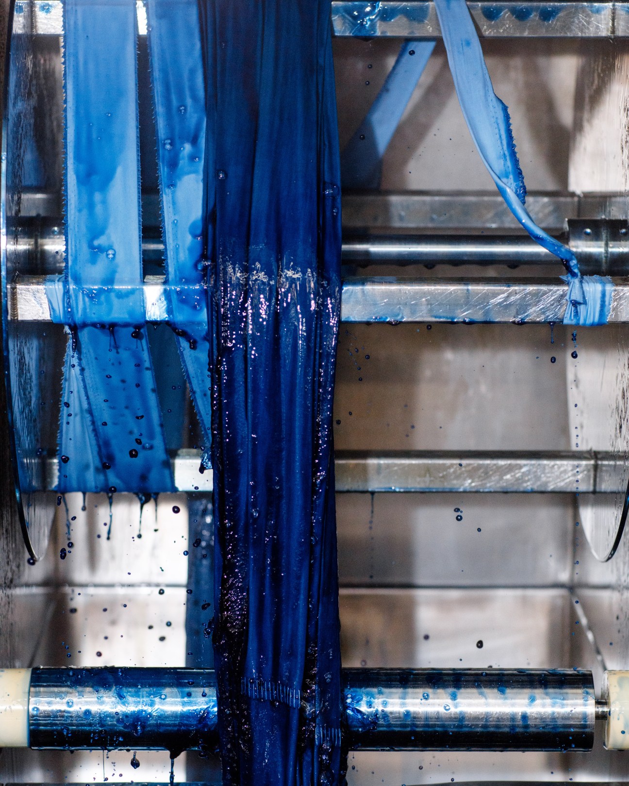 Blue dye drips from fabric suspended over industrial machinery at Pantone's facility.