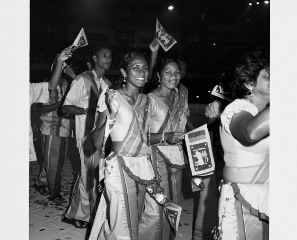 Indian track team members waving at crowds during opening ceremony parade.