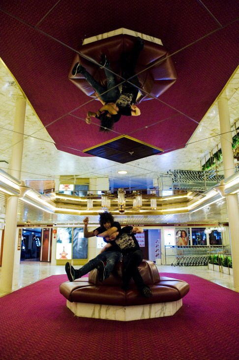 Two men playing on a brown leather circular seating in an ornate ship interior with burgundy ceiling and yellow columns.