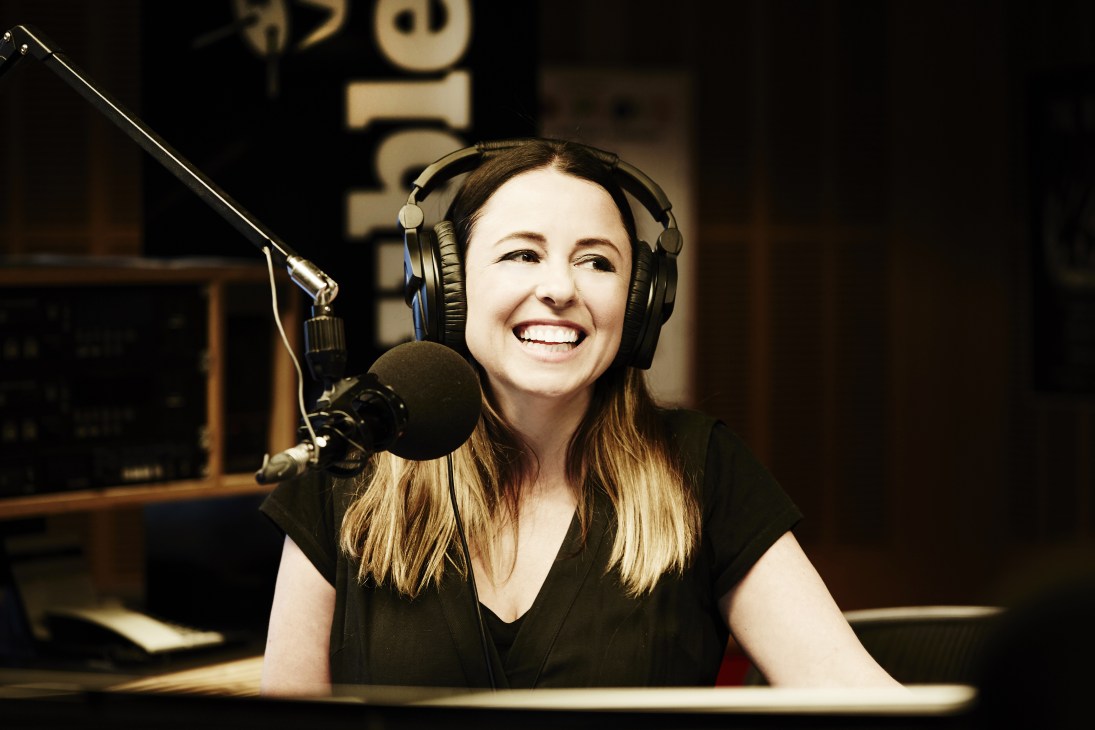 Myf Warhurst smiling at the microphone wearing headphones in a radio studio.