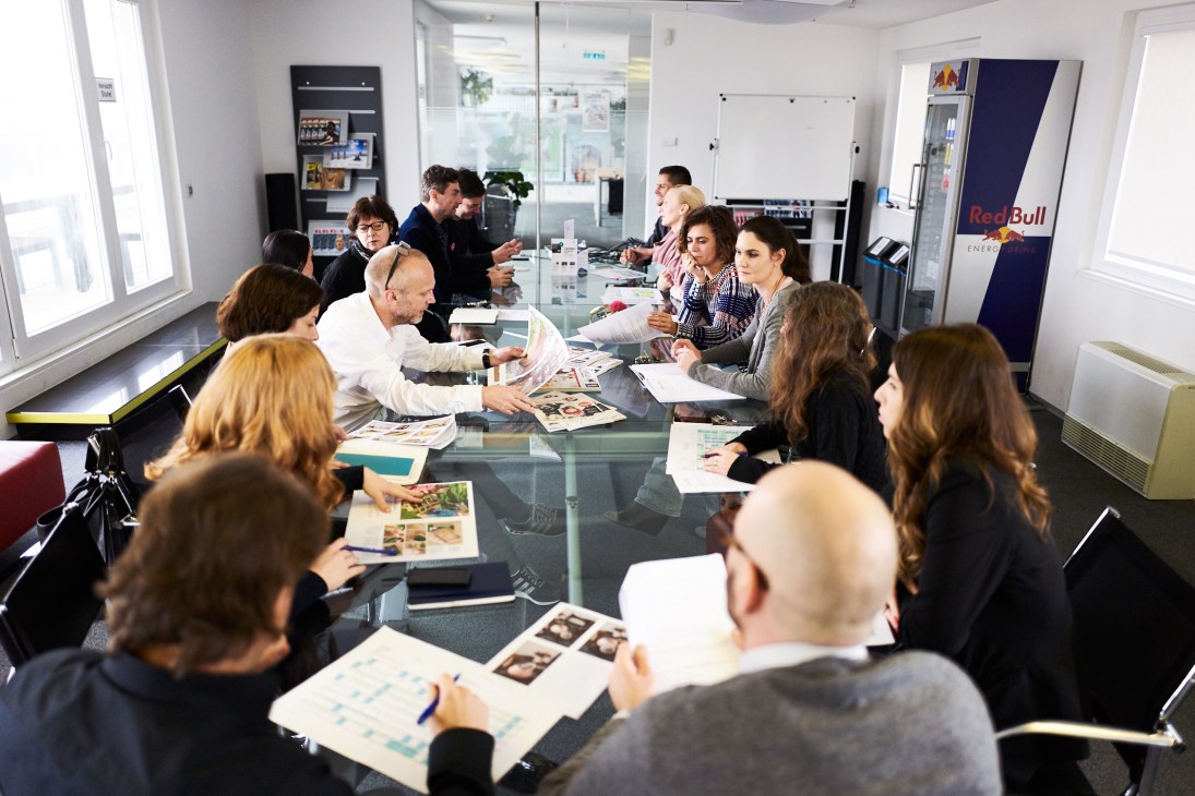 Editorial team of Servus in Stadt & Land magazine gathered around a table reviewing materials in their Vienna office.