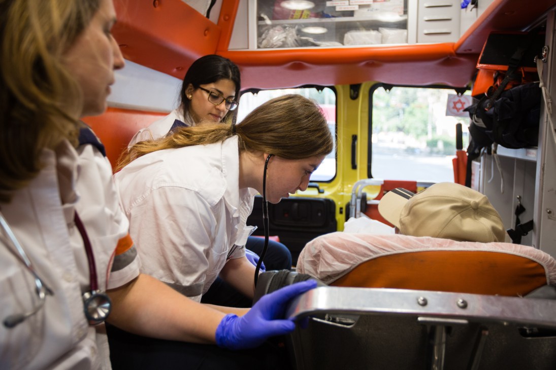 Female MDA paramedics treating a patient inside an orange and yellow ambulance.