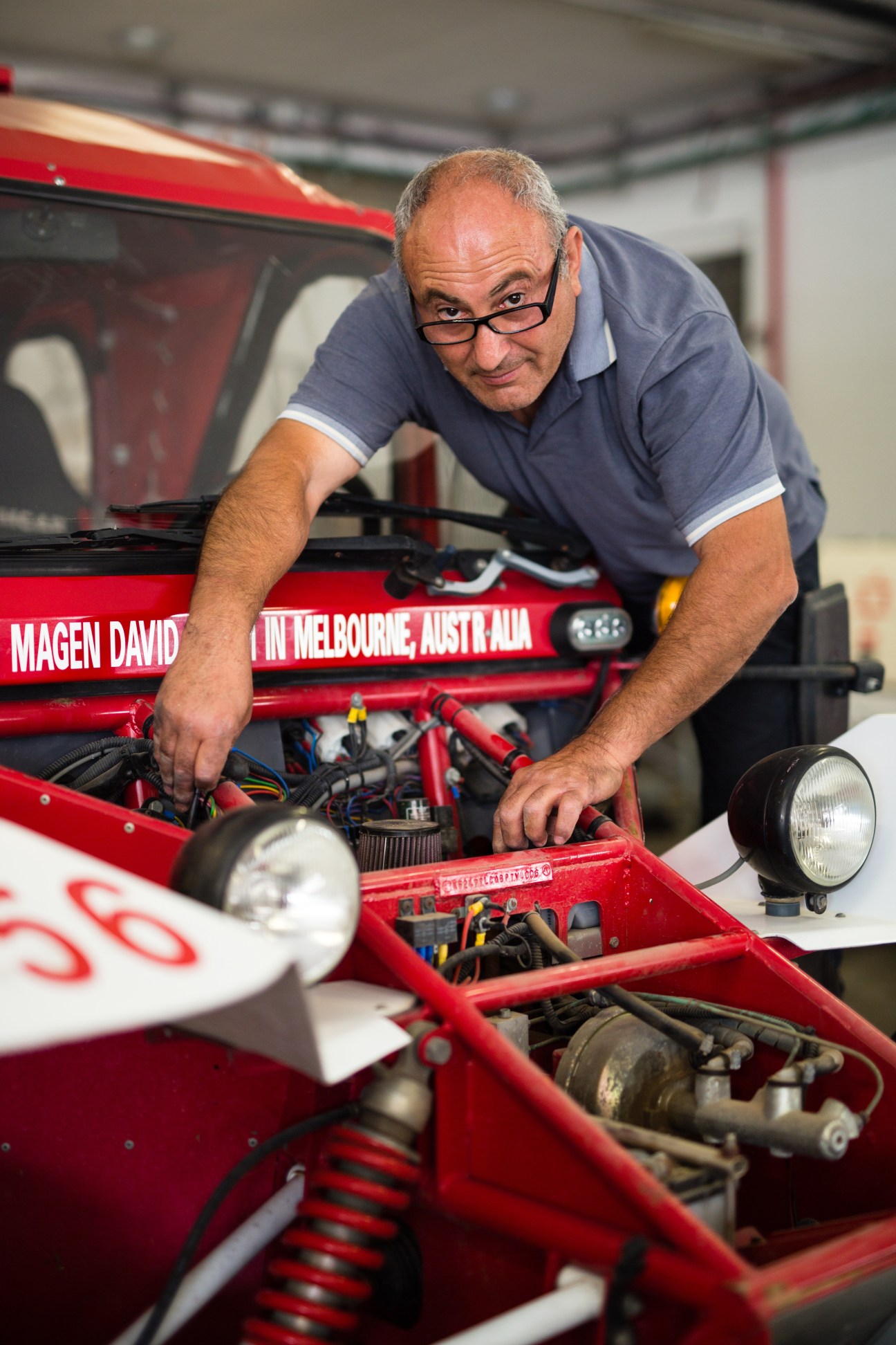 Volunteer mechanic working on a red Magen David Adom emergency vehicle engine.
