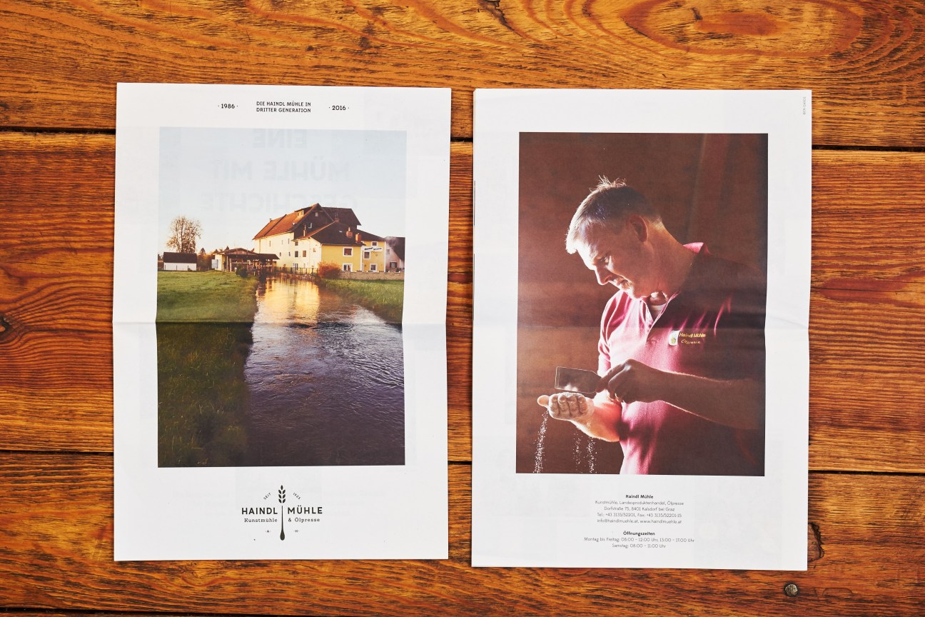 Two printed design pages displayed on wooden surface featuring Haindl Mühle branding by En Garde.