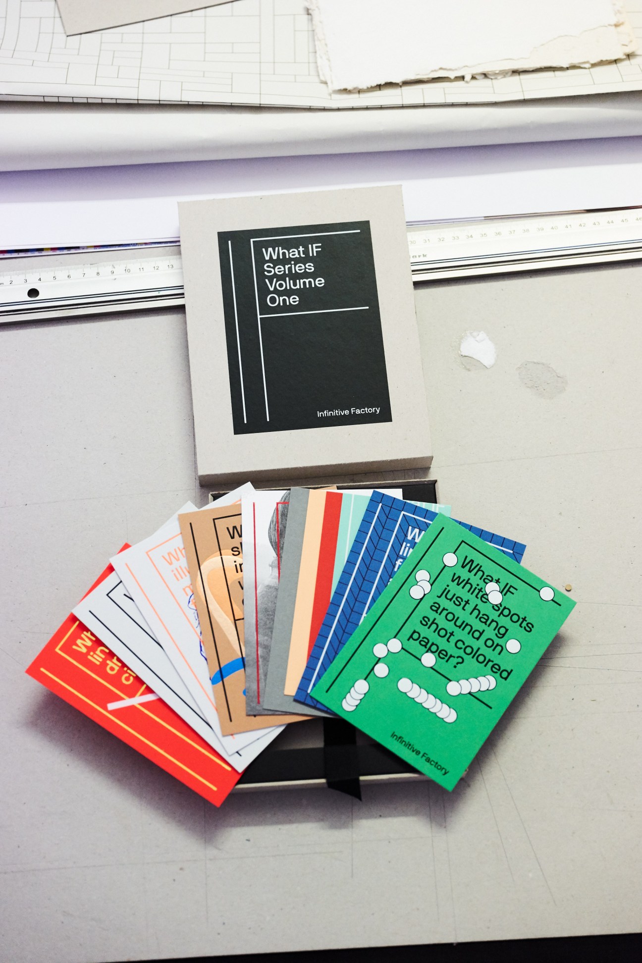 Colorful printed booklets from the 'What If' series designed by Bruch for Infinitive Factory, displayed on a design workspace.