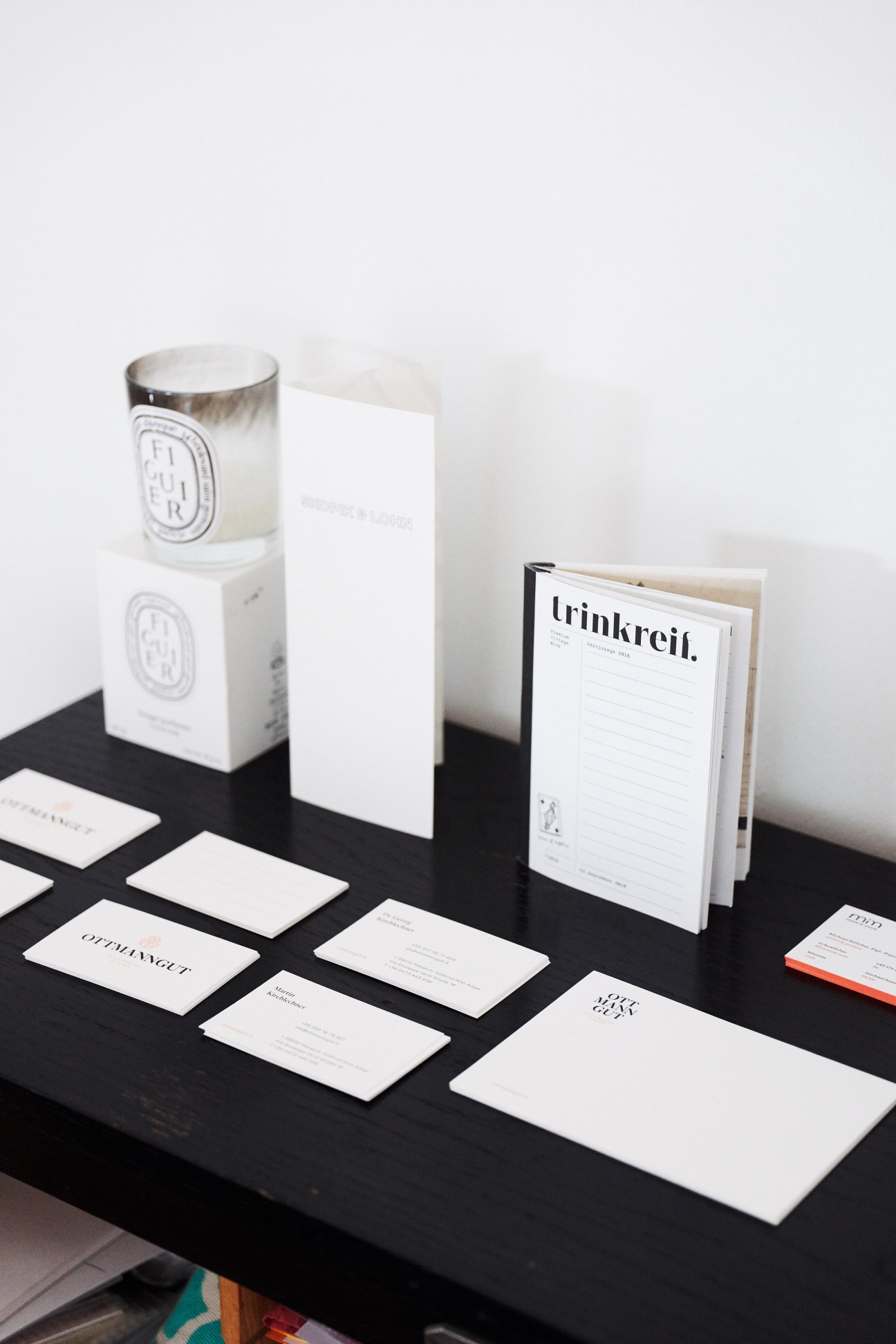 Minimalist branding materials displayed on black surface including business cards, envelope, booklet and candle.