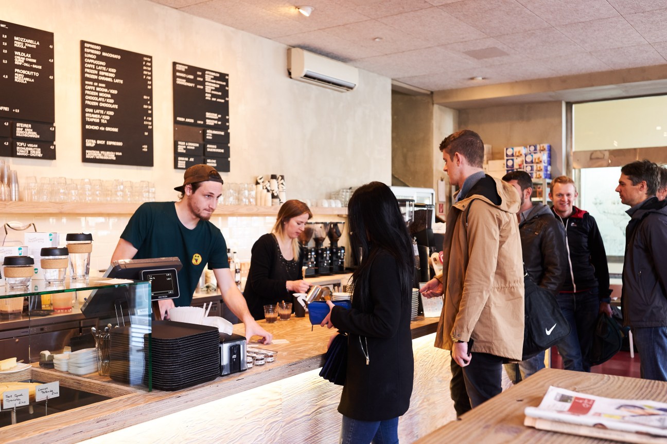 Customers ordering at the counter of Tribeka Coffee Shop with barista and menu boards on wall.