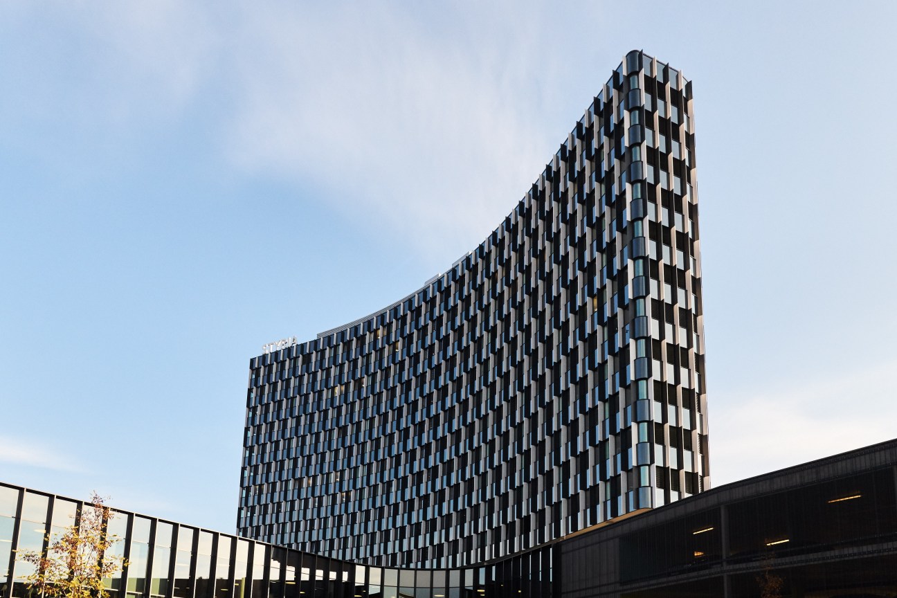 Modern curved office building with repeating window pattern and geometric facade under blue sky.