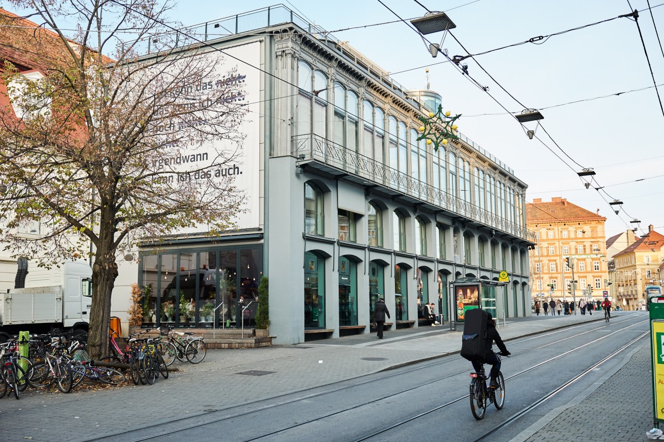 Modern Kunsthauscafe building with large windows and contemporary architecture on a Graz street with tramway.