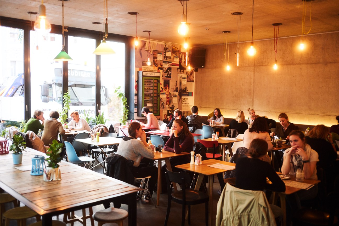 Interior of Kunsthauscafe Graz with diners seated at wooden tables under pendant lights.