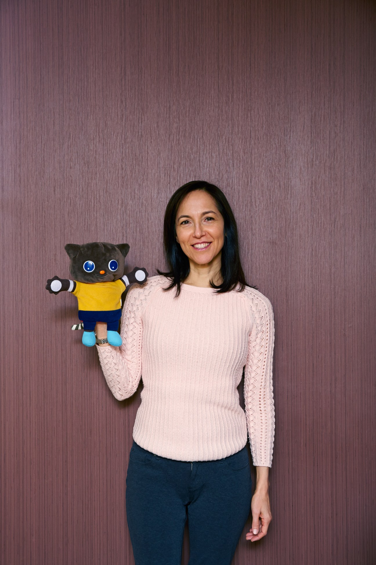 Linda Merlo from Berlitz Kids and Teens holds a black cat plush toy with yellow shirt against purple background.