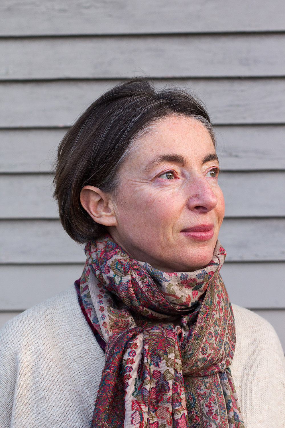 Portrait of Emma Sky, a woman with dark hair wearing a patterned scarf against a gray wooden background.