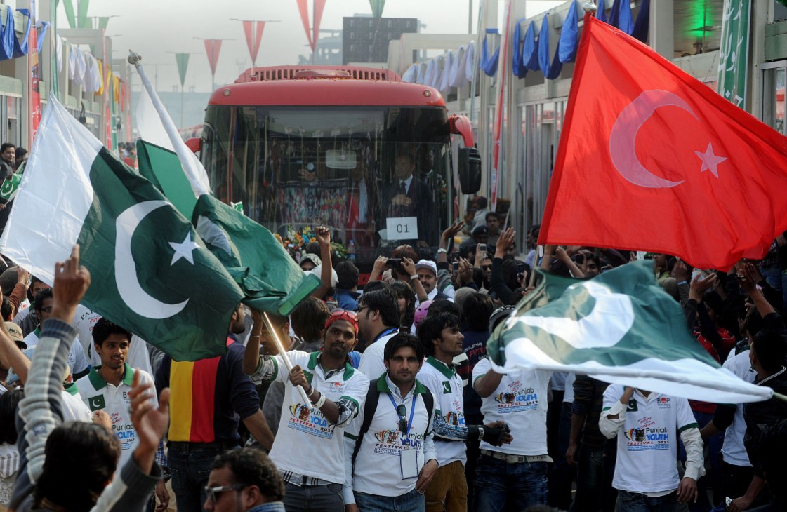 Crowd of Pakistani youth waving Pakistani and Turkish flags at a public gathering in an urban street.