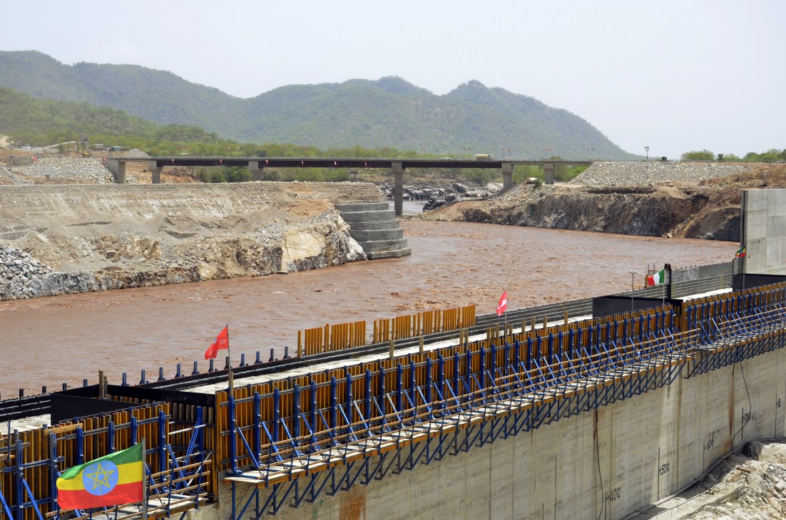 Grand Renaissance Dam construction site on the Blue Nile in Ethiopia with flags and metal scaffolding in foreground.