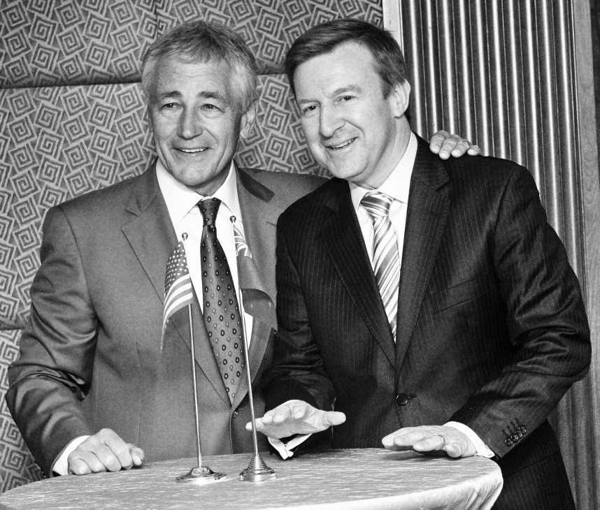 Chuck Hagel (left) and another man in suits at a formal event with microphones.