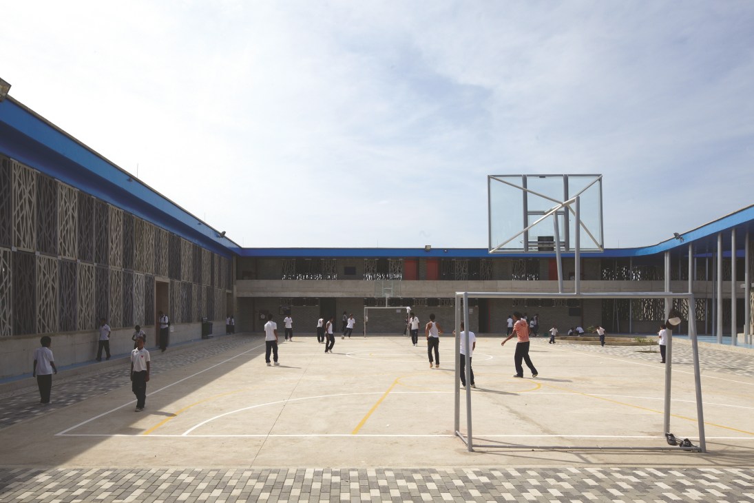 Students play in a sunny courtyard surrounded by concrete fretwork walls at Wada kindergarten in Japan.