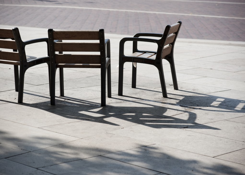 Modern black chairs with wooden seats arranged on a paved public square with geometric patterns.