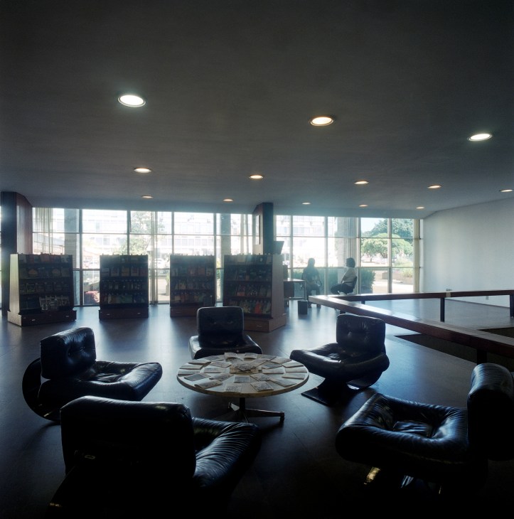 Modern reception area with black leather seating, round table, bookshelves and floor-to-ceiling windows overlooking landscaped grounds.