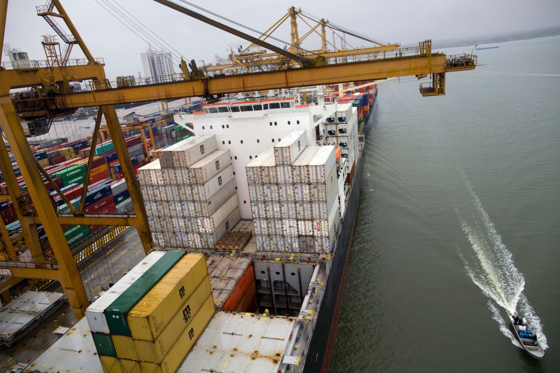 Cargo ship loaded with stacked shipping containers at Buenaventura port with yellow cranes and machinery overhead.