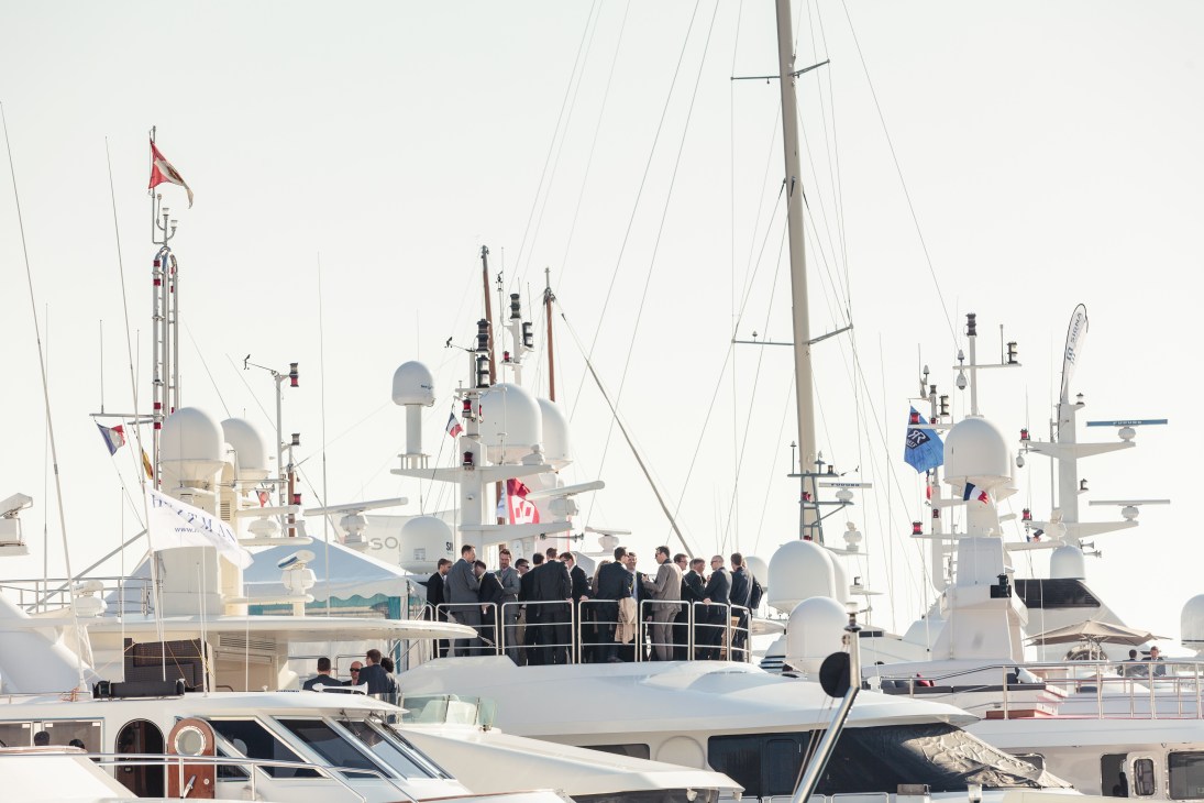 Executives in suits gathered on the deck of a luxury yacht moored in Cannes marina.