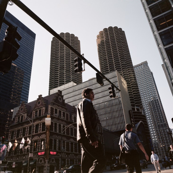 Marina City's twin cylindrical towers rise above Chicago street with pedestrians walking below.