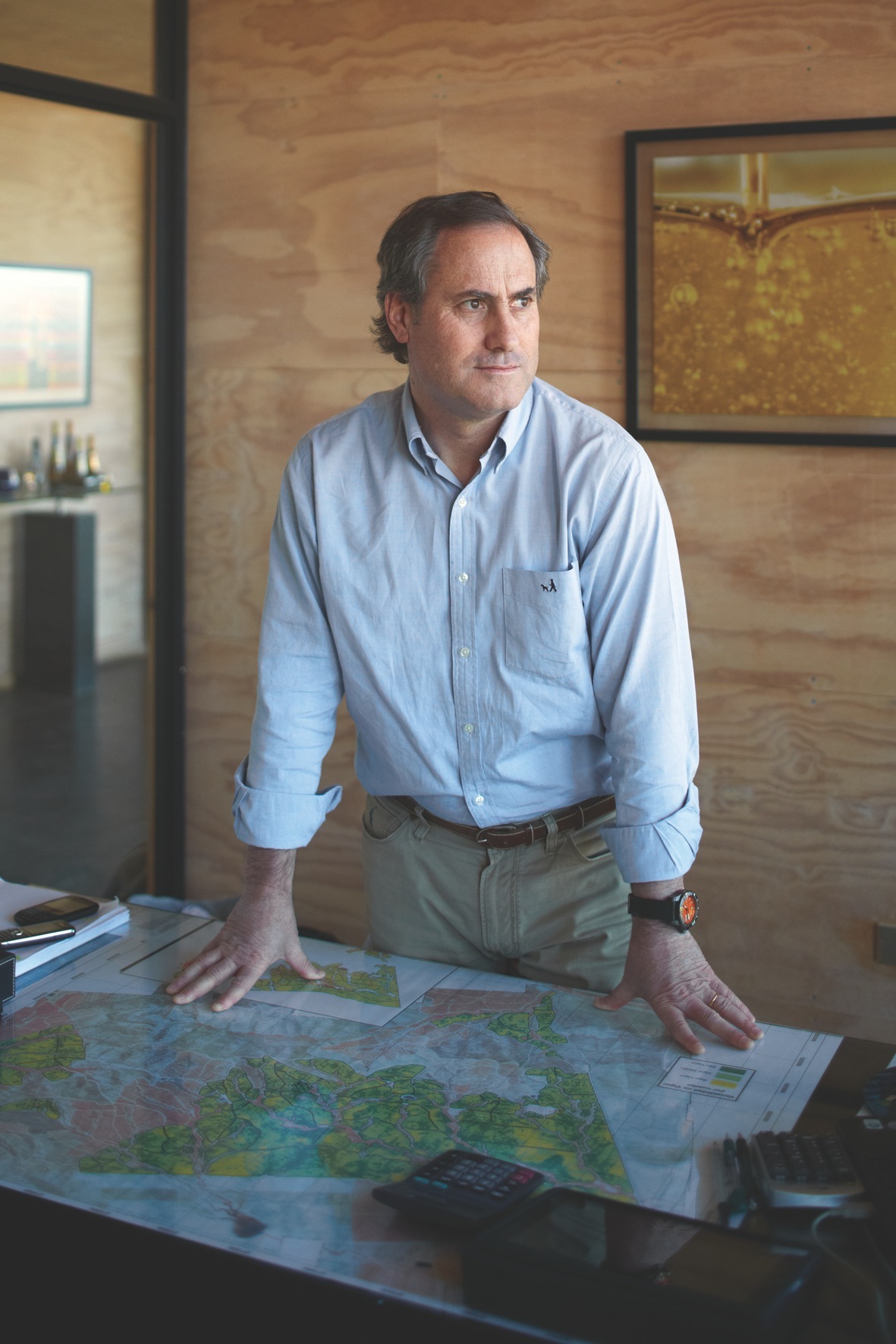 Man in light blue shirt standing at table with maps in wood-paneled office