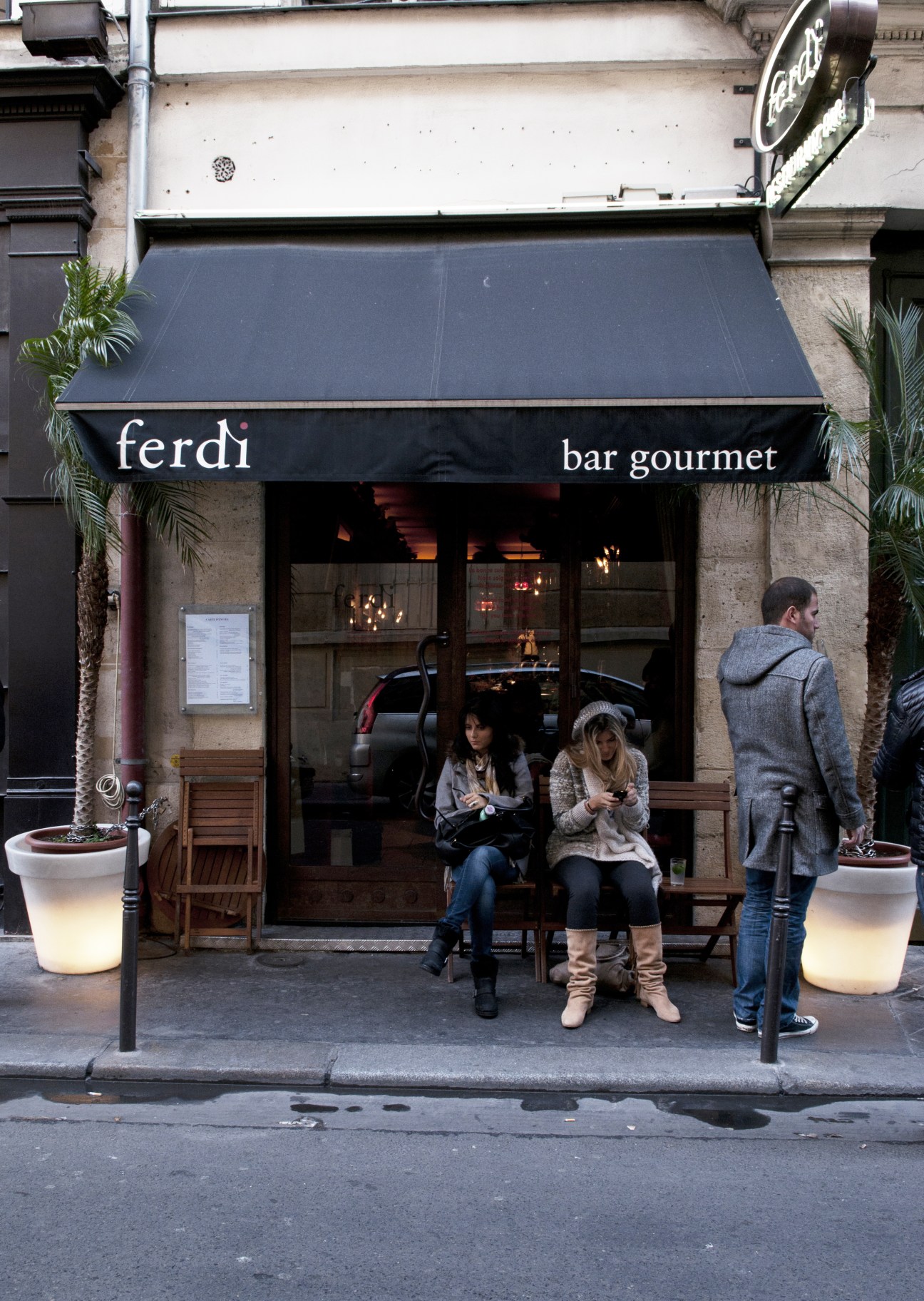 Ferdi bar gourmet storefront in Paris with black awning, wooden seating, and people sitting outside.