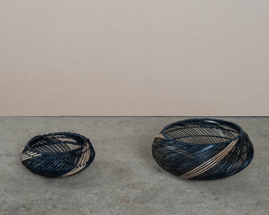 Two woven baskets with black and natural fiber in oval shapes on concrete floor.