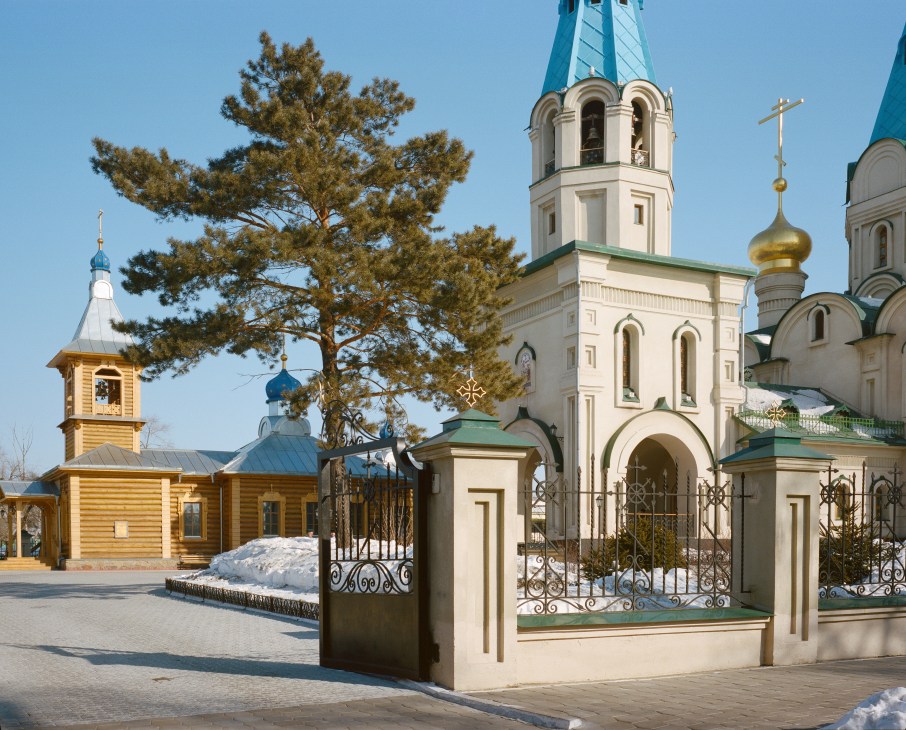 Orthodox cathedral in Blagoveshchensk with white walls, turquoise domes and golden crosses surrounded by evergreen trees and snow.