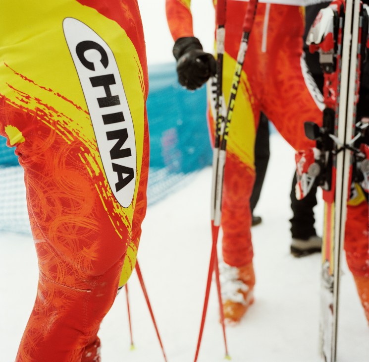 Close-up of red and yellow China ski pants and equipment laid out on snow.