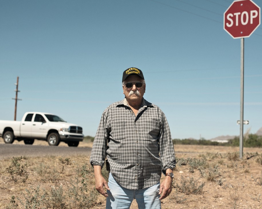 Al Garza of the Patriot's Coalition stands in desert landscape wearing a cap and checkered shirt.