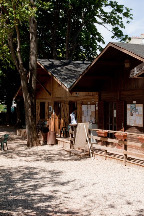 Wooden pavilion with large trees and outdoor seating area in a Parisian garden.