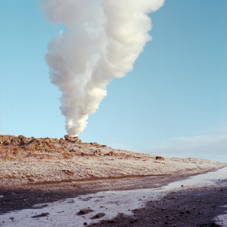 Steam rising from geothermal activity on an Icelandic beach under blue sky.